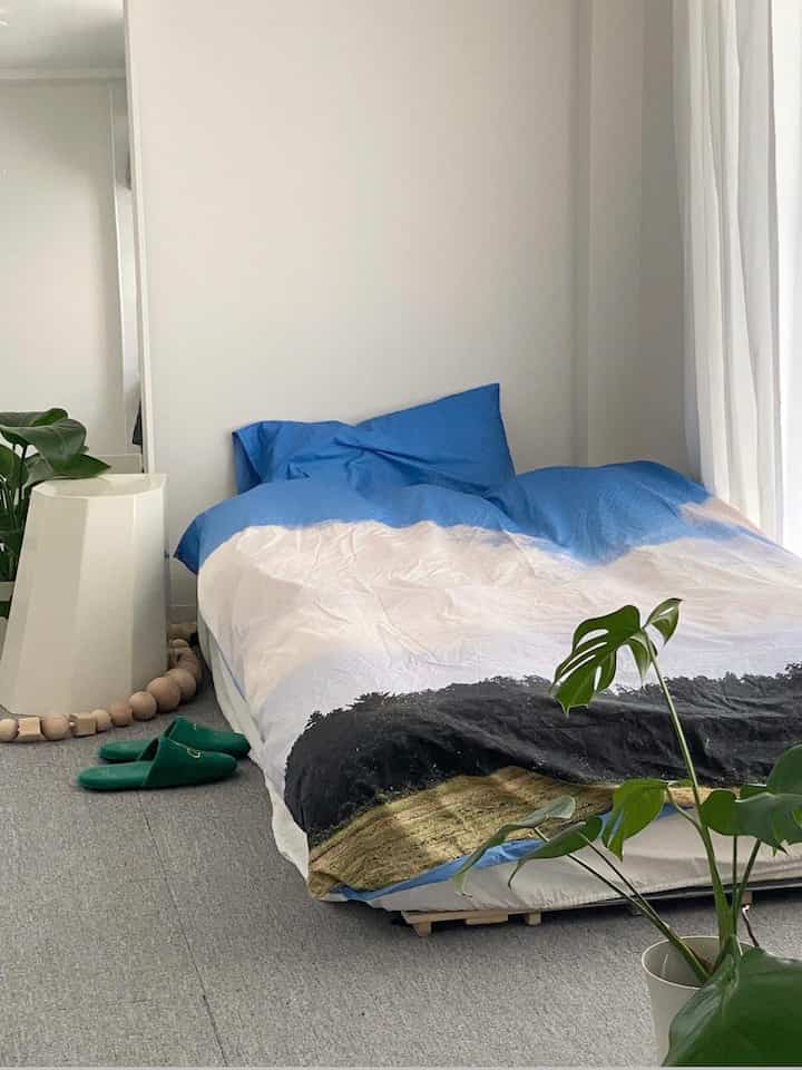 落ち着いたナチュラルトーンの寝室、低いフレームのベッドと自然柄のブランケットが配置されたミニマルなインテリア