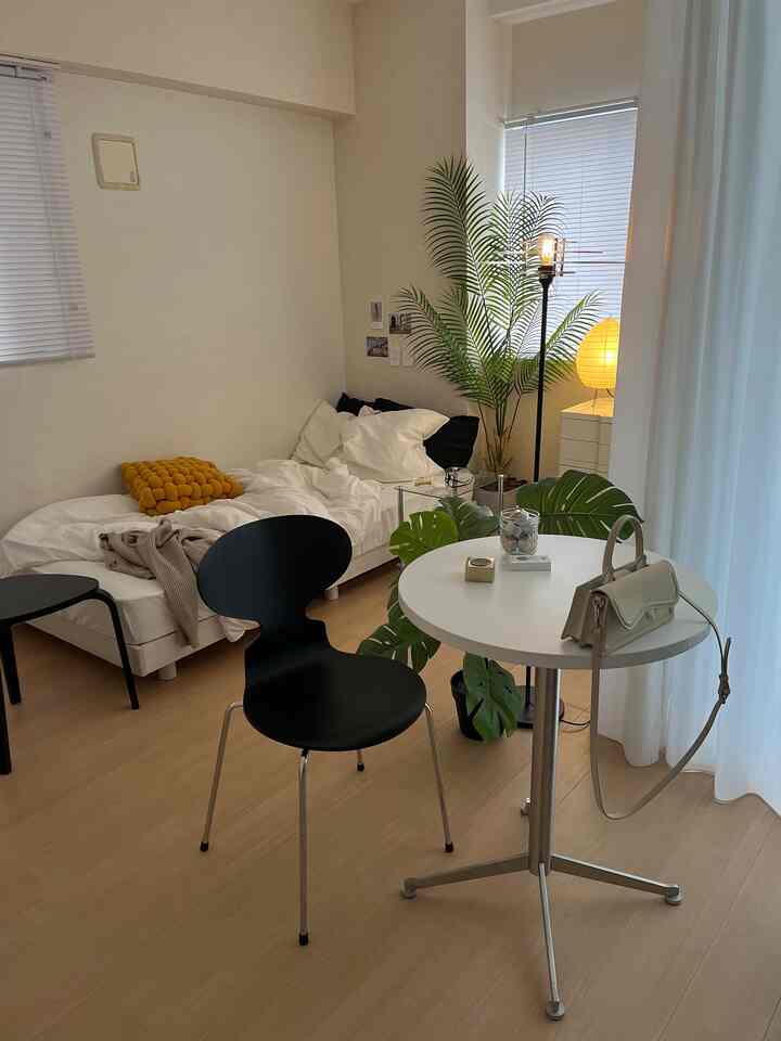 Bedroom space in white and natural color tones featuring a white bed, black chairs, a small round table, and green plant with cozy atmosphere