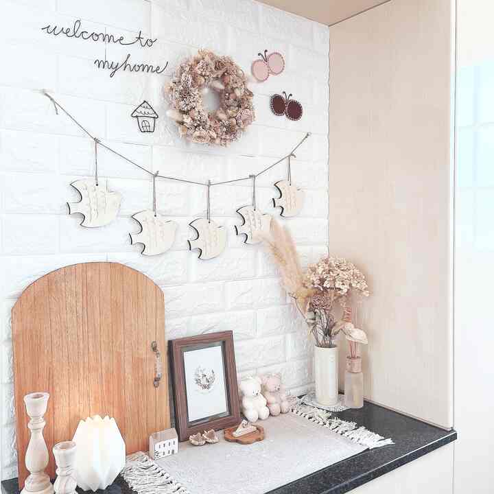 白いレンガ調の壁とナチュラルウッド調の玄関、鳥の壁掛け飾りやドライフラワー、キャンドルが配置された雰囲気のあるインテリア