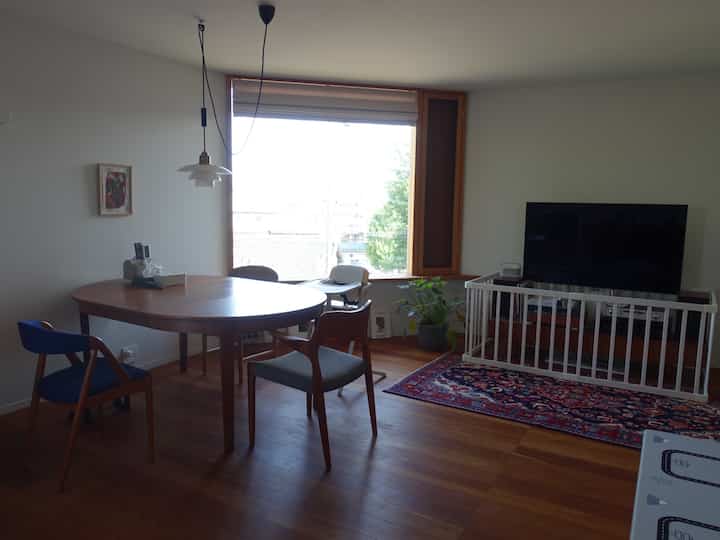 Natural wood-toned dining and living room featuring an oval table, baby high chair, and safety gate for family-friendly environment