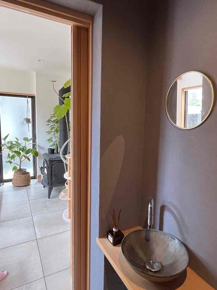 ナチュラルカラーと木目調が調和した縦長の玄関、丸い鏡と洗面台が配された印象的な空間