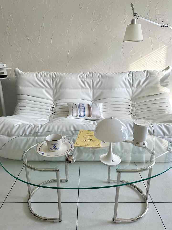 Bright white-toned small living room featuring a transparent glass coffee table and a simple design sofa with a tidy ambiance