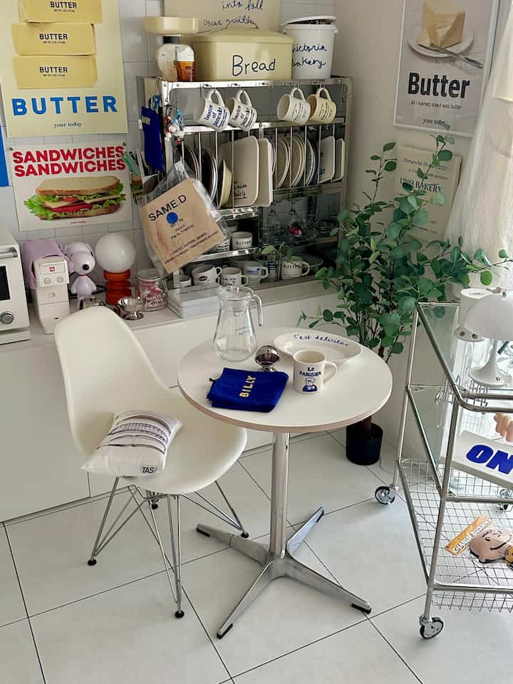 白を基調としたキッチン空間、丸いダイニングテーブルと椅子、食器収納とキッチンワゴンが配置されたすっきりとしたホームカフェの雰囲気