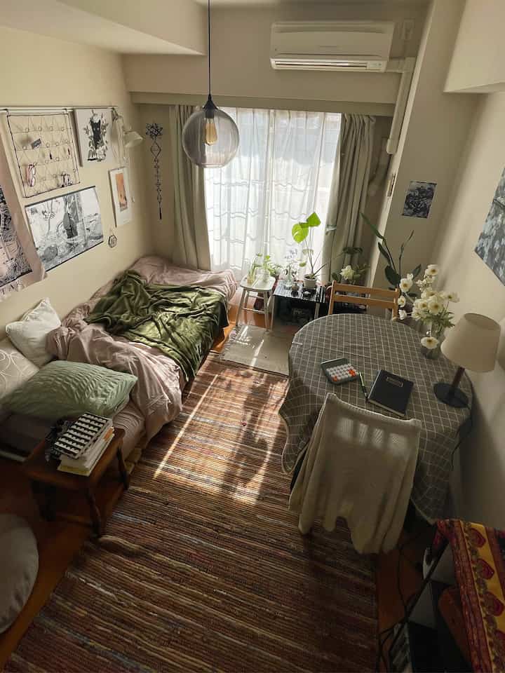 Beige-toned small bedroom featuring a single bed, round table, plants, and natural decor creating a cozy atmosphere