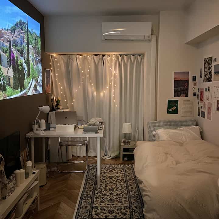 ホワイトとウッドトーンの一人暮らし用寝室兼ホームオフィス、プロジェクタースクリーンとカーテンのライトが印象的な雰囲気のあるインテリア