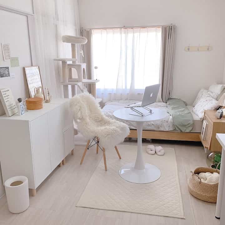 Bright white and natural wood-tone compact bedroom featuring a round table and cat tower in a cozy single household space