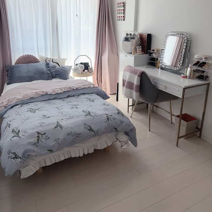 ホワイトとピンクのトーンのカーテンとゴールドの脚のコンソールテーブルが配置された、居心地の良い寝室