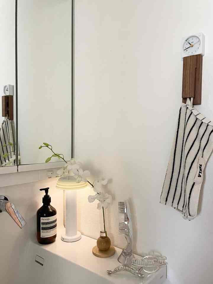 白とシルバーの落ち着いた浴室、木製アクセサリーとテーブルランプが温かみある雰囲気を演出するインテリア