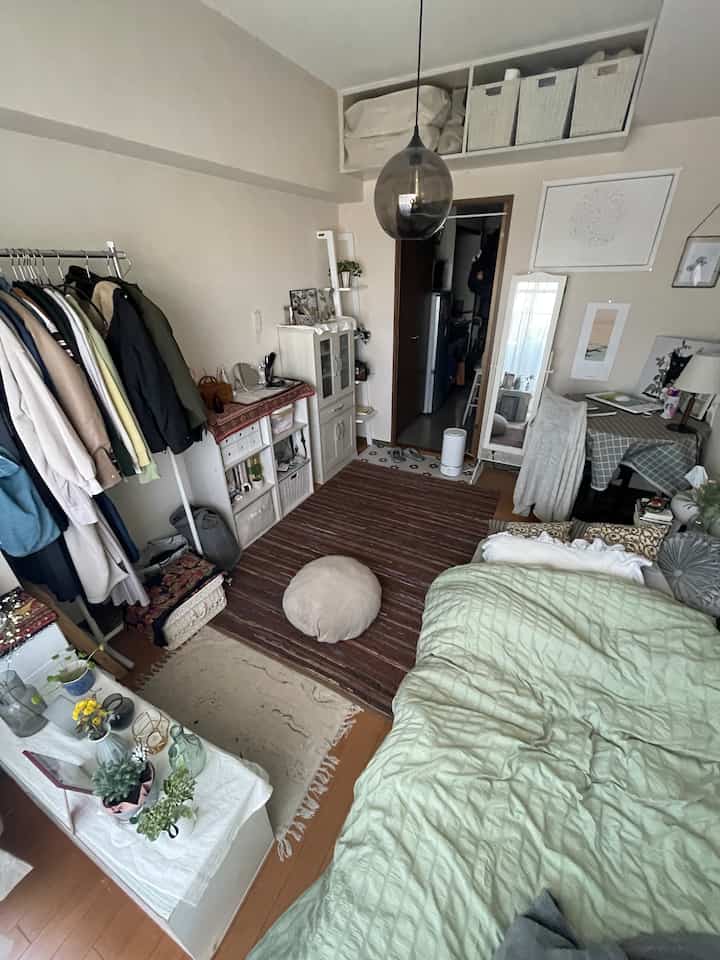 ナチュラルカラーの狭い寝室、ベッドとコートラック、ペンダントライトが配置された雰囲気のあるインテリア