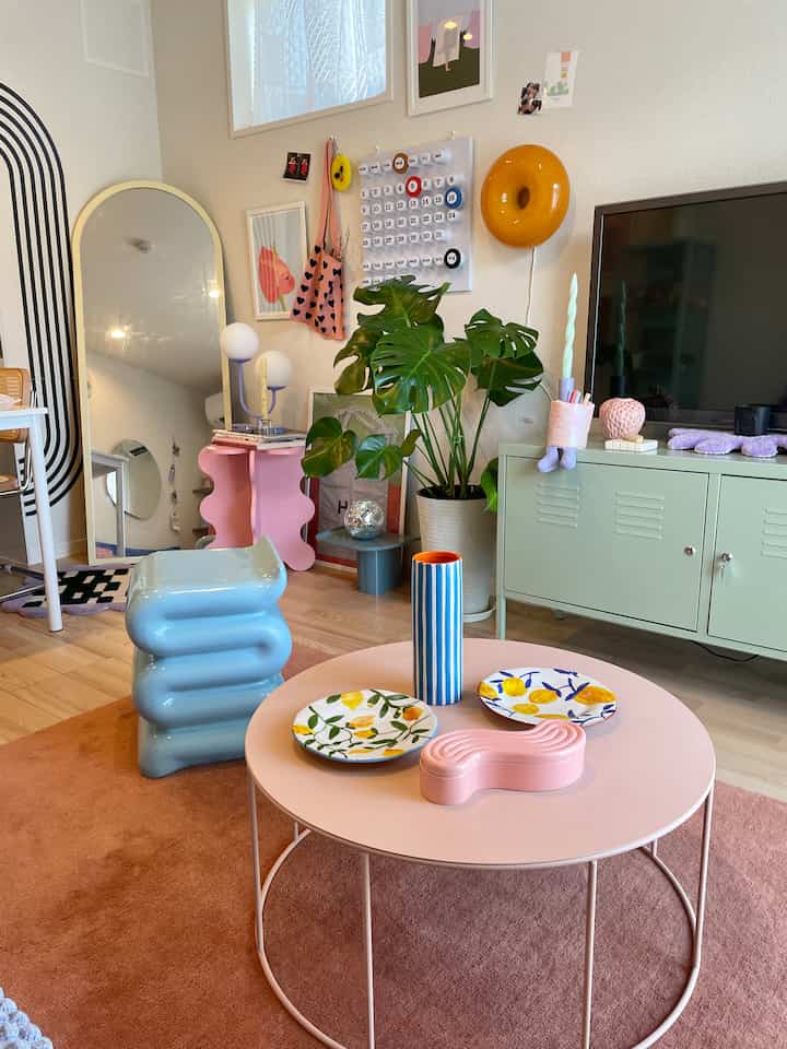 パステル調のリビング、ピンクのコーヒーテーブルとミント色のテレビ台、植物と多彩な装飾が印象的な空間