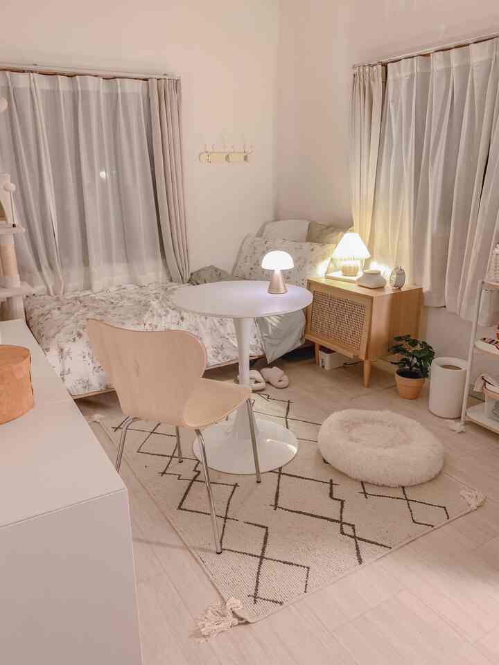 Cozy small bedroom with warm beige and wood tones, featuring floral bedding, a mirror, and a round table