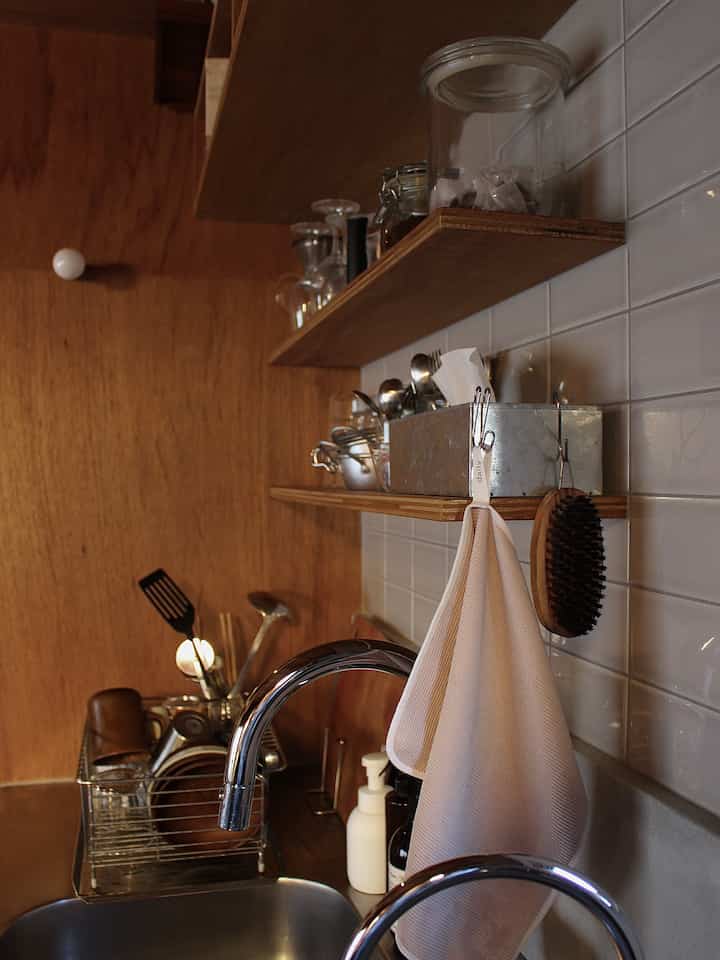 白いタイルの壁と木製の棚が配置された居心地の良いキッチン、シンクと整頓されたキッチン用品が特徴的な空間