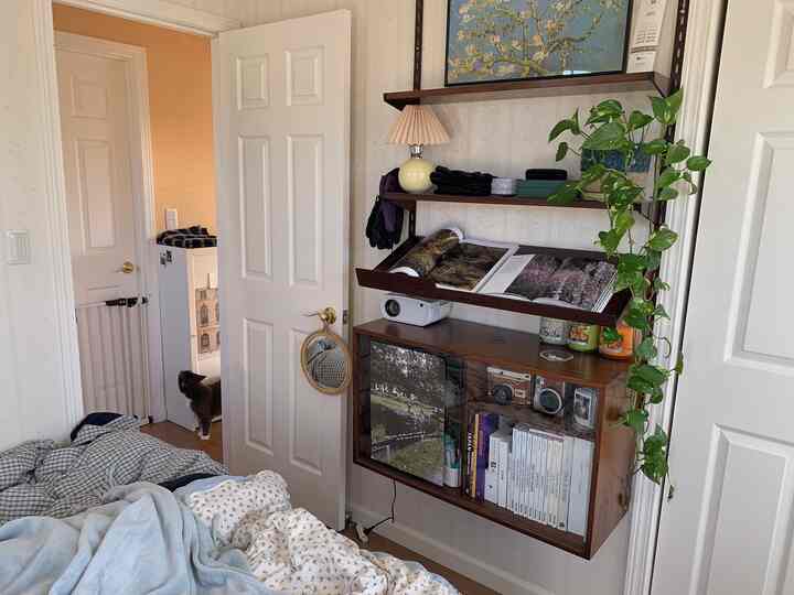 白い壁とドアが際立つ寝室、木製の棚と植物が配置された雰囲気のあるインテリア