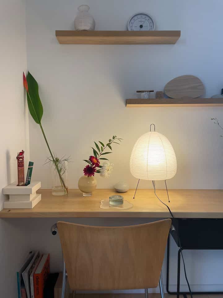 明るくナチュラルなトーンのホームオフィス、木製デスクと花瓶、テーブルランプが配置されたシンプルな雰囲気のインテリア
