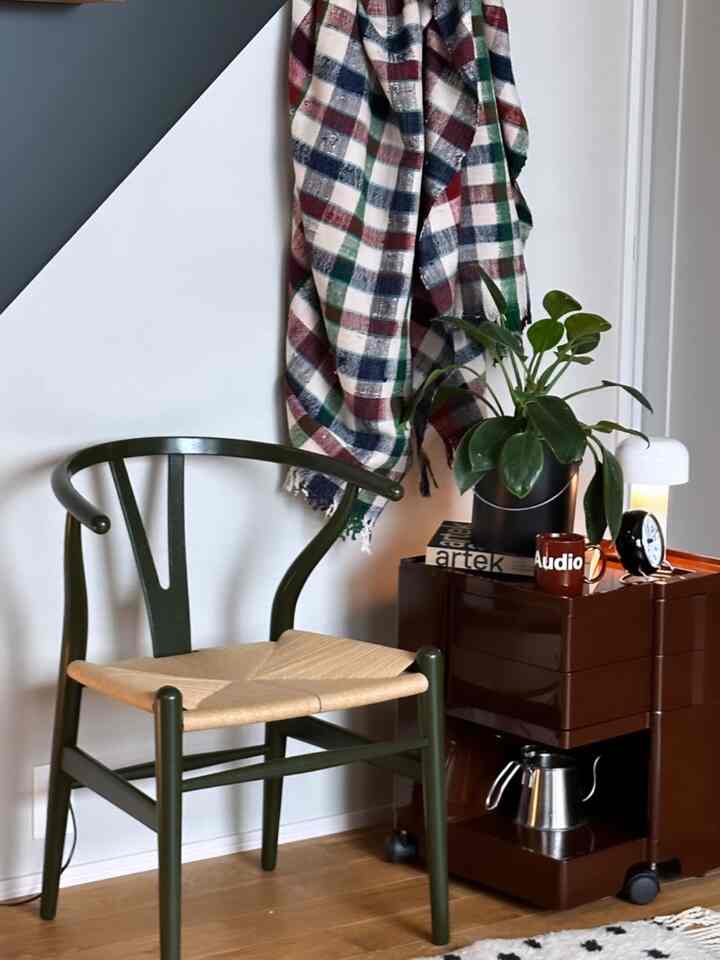 Room with natural tones featuring an olive chair, vintage brown Boby wagon, table lamp, and potted plant creating cozy atmosphere