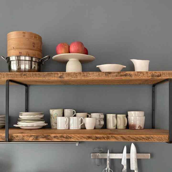 A kitchen with gray walls and wood-tone shelves showcasing neatly arranged white dishes and cups in a tidy setting