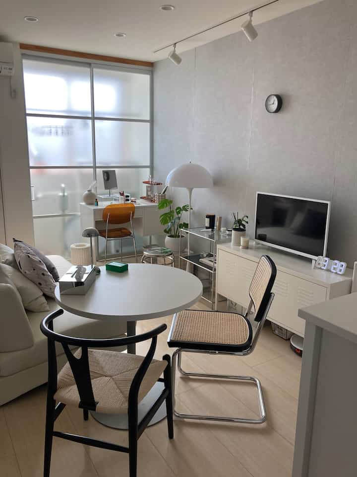 白とナチュラルカラーの小さなリビング、丸テーブルとラタンチェアが配置されたカフェ風インテリア