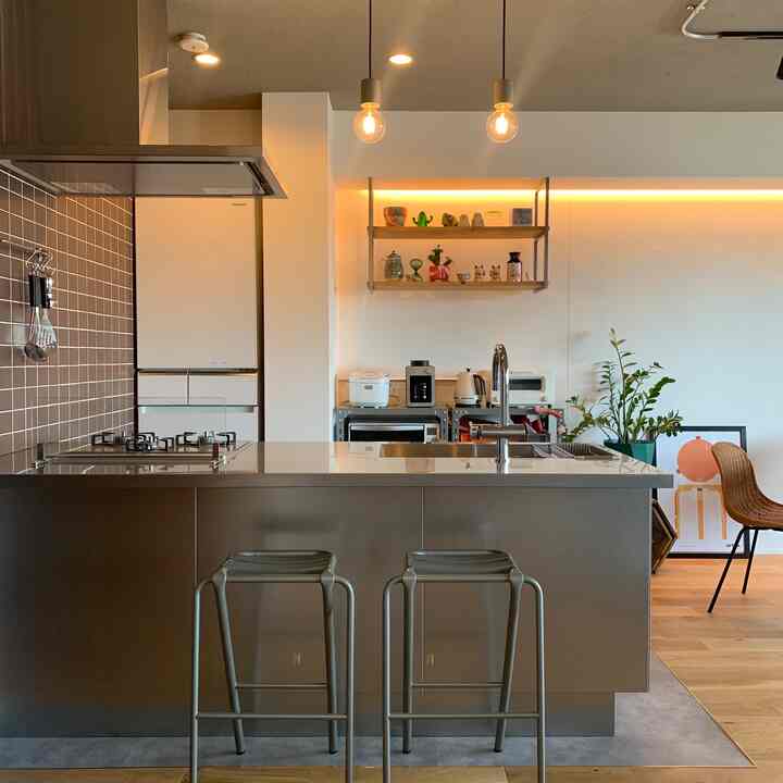 ステンレスと木目調が調和したミッドセンチュリーモダンのキッチン、カウンタースツールとペンダントライトが配置された洗練された空間