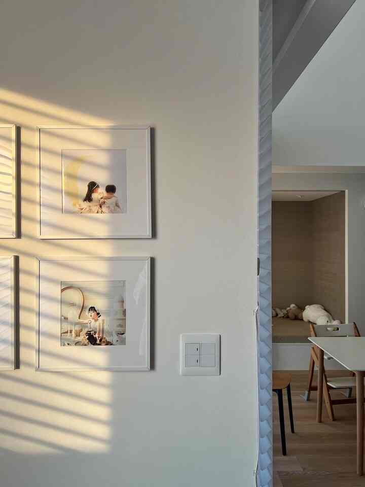 温かみのあるナチュラルな色調のダイニングルーム、白い壁に赤ちゃんの写真額が配置された印象的な空間