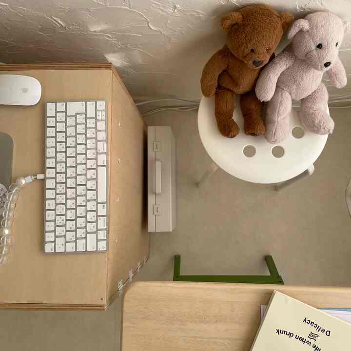 ホワイトのスツールの上に茶色とベージュのクマのぬいぐるみが二つ置かれた、居心地の良いナチュラルな雰囲気のホームオフィス空間