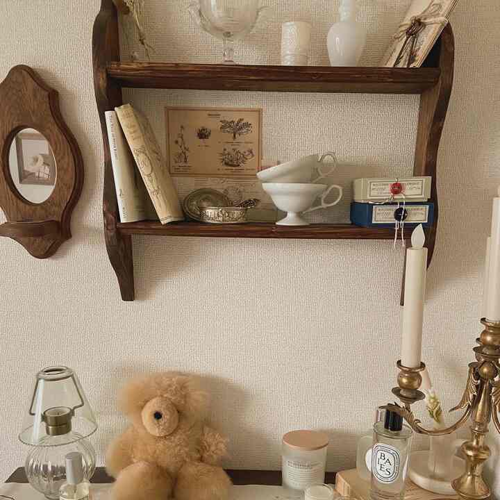 ベージュとブラウンの色調が特徴的なヴィンテージ風リビングルームで、木製の棚とキャンドルホルダー、ぬいぐるみのクマが配置された温かみのあるインテリア