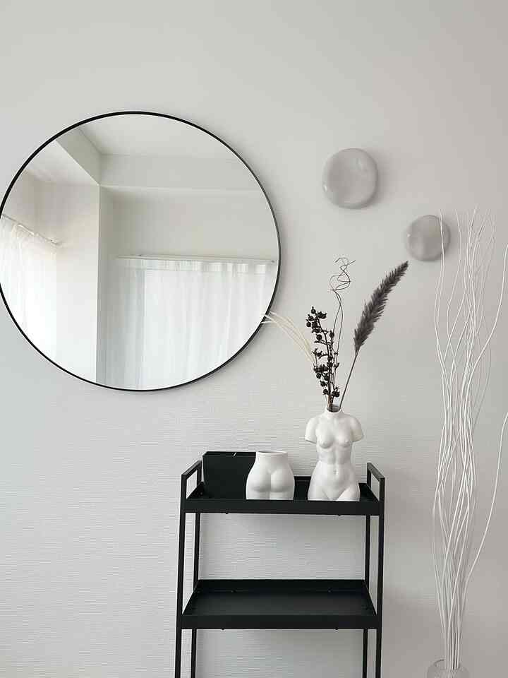 Monotone minimalist space featuring a black metal cart, round mirror, and female torso vases arranged simply