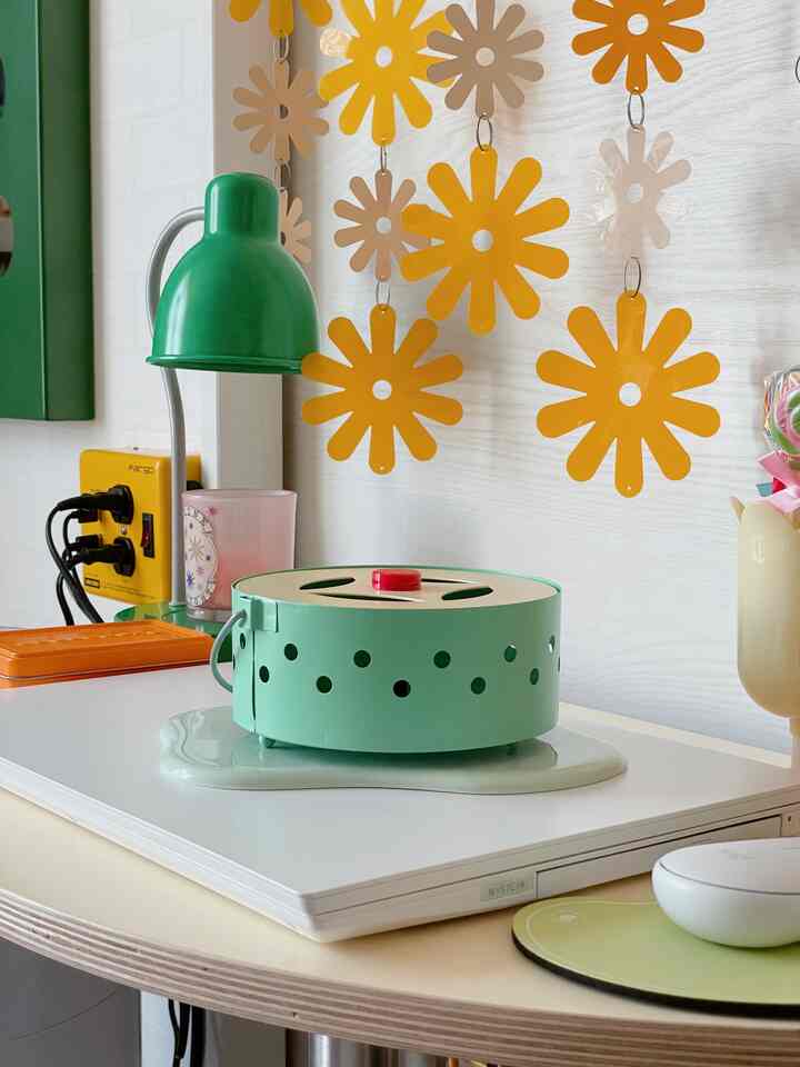 ミント色と黄色を基調としたデスク上に、レトロ感のある蚊遣り器と黄色の花形モビールが配置された雰囲気のあるインテリア