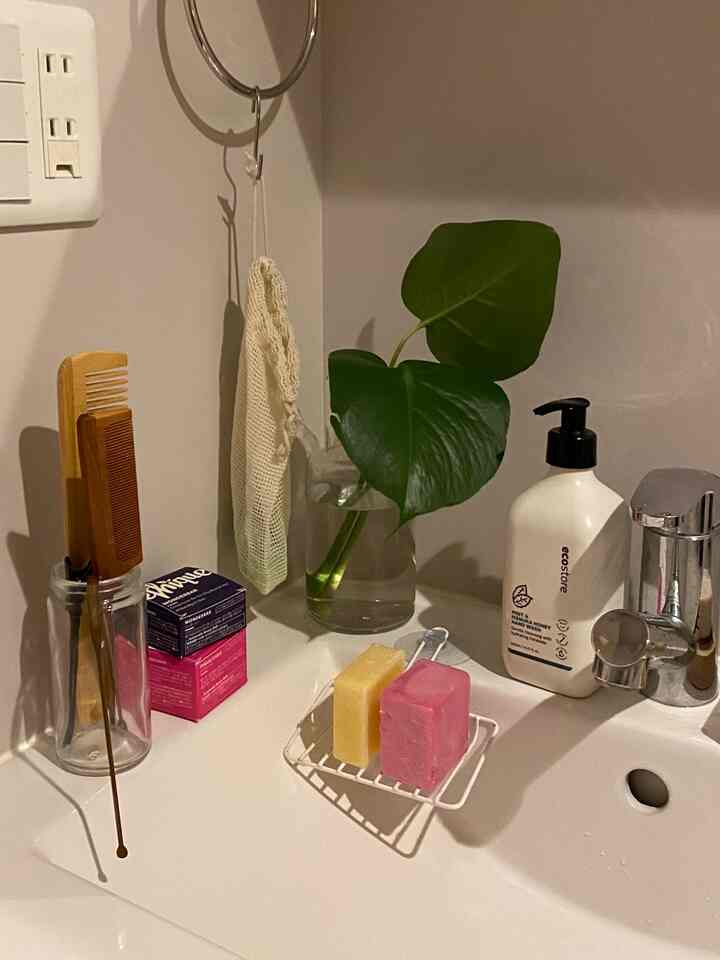 White bathroom sink area featuring a glass vase with green leaves and colorful soap bars, creating a natural atmosphere