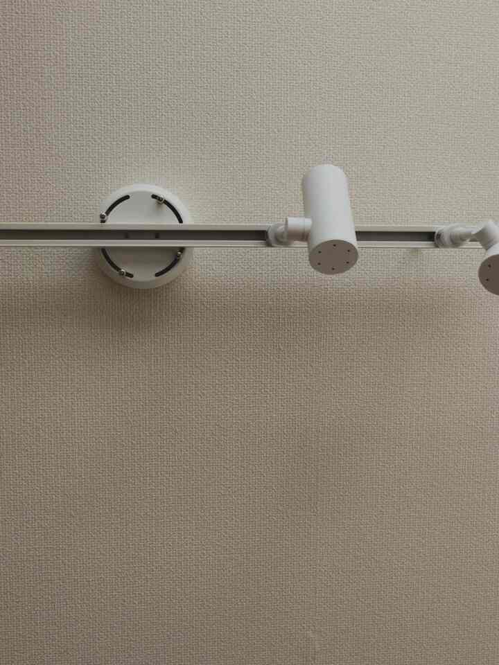 ダークグレーの壁に取り付けられたシルバーのダクトレールと2つの白いスポットライトがあるシンプルな照明インテリア