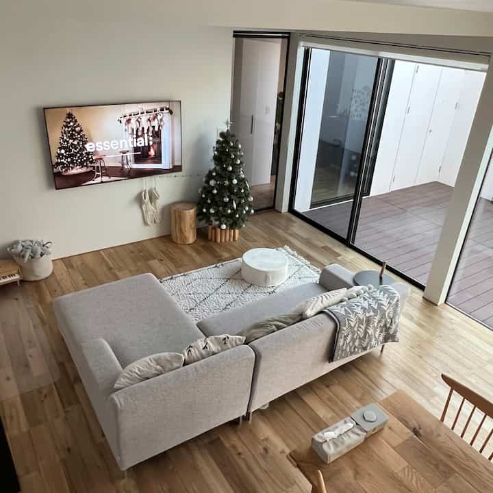 ナチュラルトーンのリビング、ライトグレーのソファと木目調の床、クリスマスツリーとラグが配置された雰囲気のあるインテリア