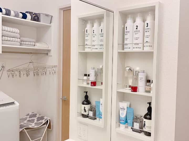 グレーとホワイトのトーンのバスルーム兼ランドリールーム、大きな鏡と整然としたタオルや洗面用品が配置されたシンプルな空間