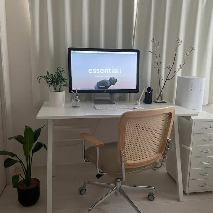 明るいホワイトトーンのホームオフィス、シンプルなデスクと木目調のオフィスチェア、植物が配置された落ち着いた雰囲気のインテリア