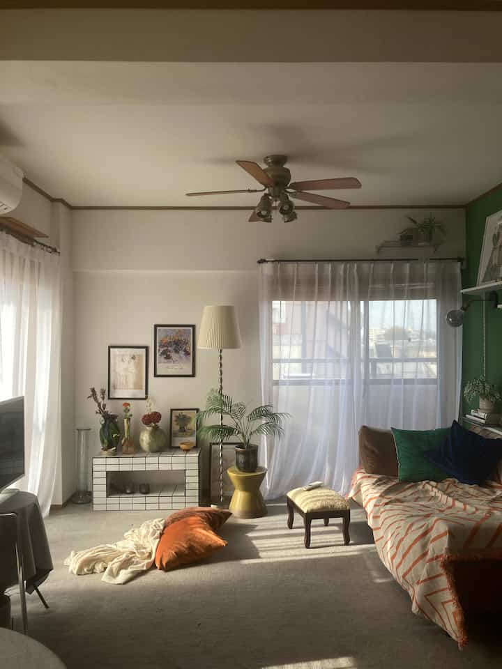 白と緑のトーンが印象的なリビング、ソファやカーテン、フロアランプが配置された自然な雰囲気のあるインテリア