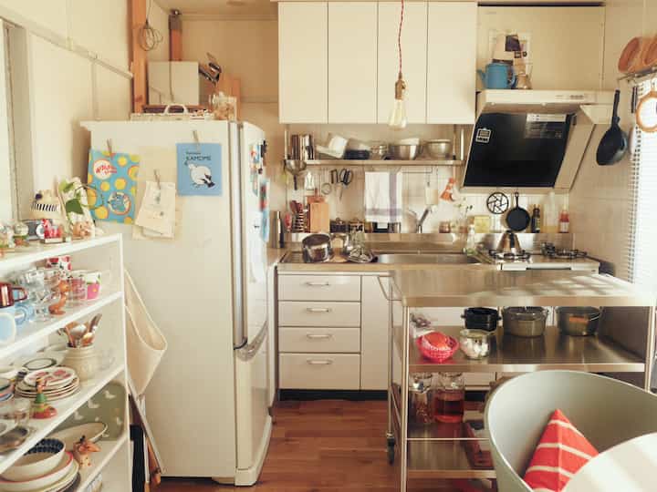A compact kitchen space featuring white and wood tones, multiple storage cabinets and a kitchen cart arranged for cozy functionality