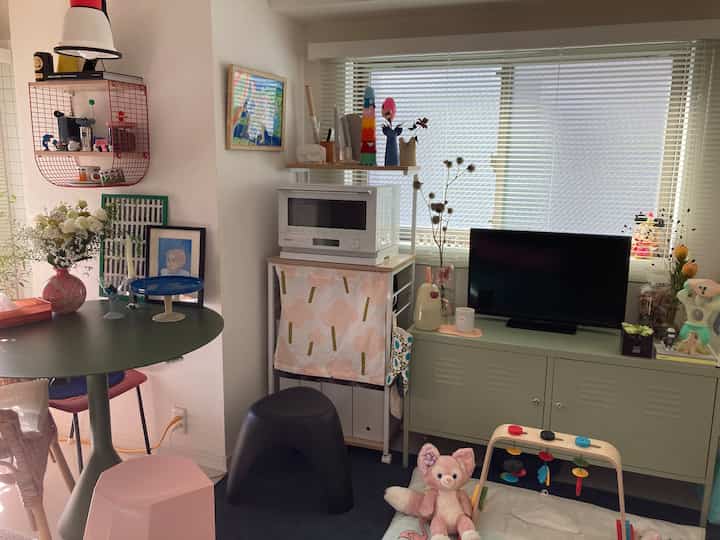 ピンクと黒のアクセントのあるリビング兼キッチンコーナー、収納とペット用おもちゃが配置された多目的な雰囲気のある空間