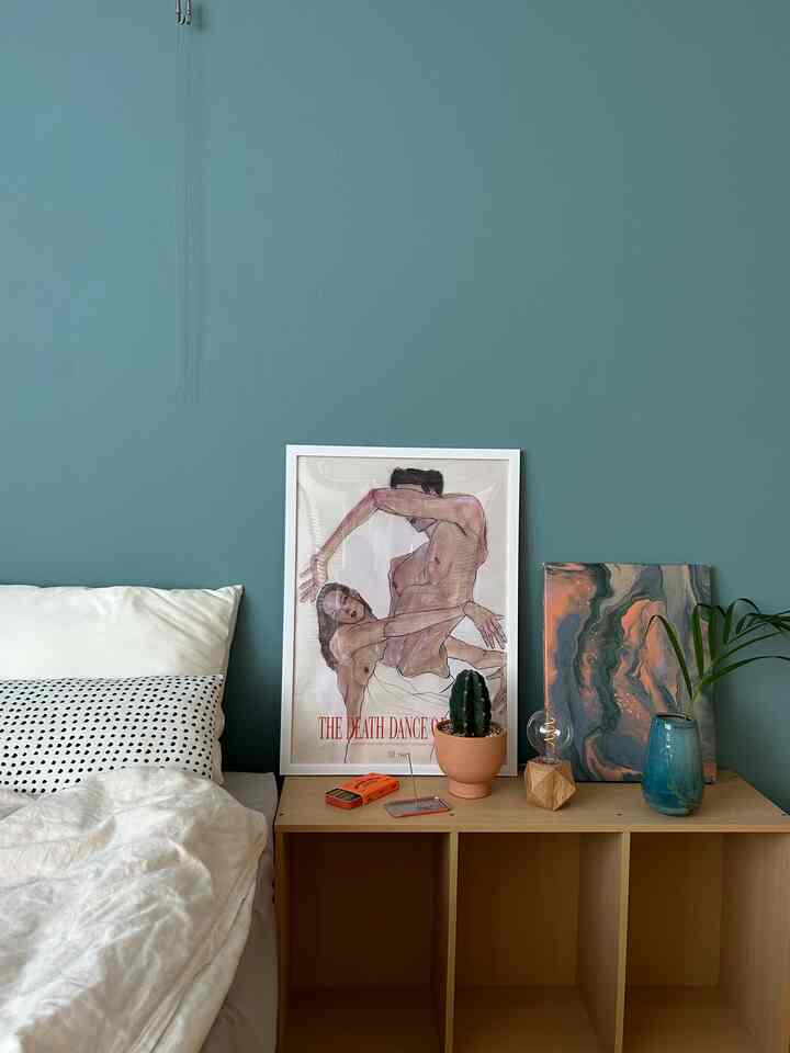 Green-toned wall and beige furniture in a bedroom featuring art frames and incense sticks arranged for a cozy atmosphere