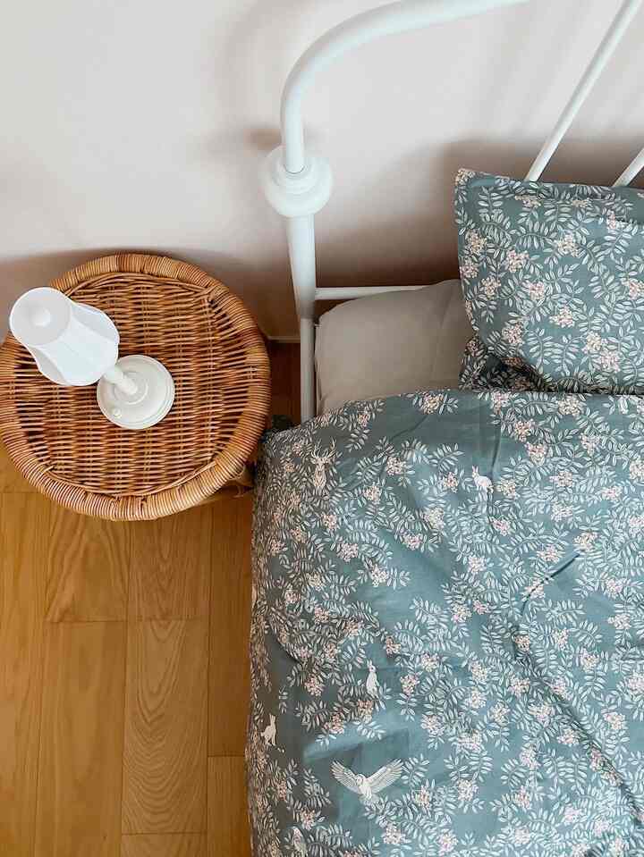 白いベッドと木目調の床、ラタンのナイトテーブルが配置されたナチュラルな雰囲気の子供部屋