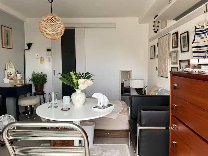 ホワイトトーンとナチュラルな雰囲気の小さなダイニングルーム、中央に花瓶と装飾が置かれた丸いテーブルと黒い革のアームチェアが配置された落ち着いた空間