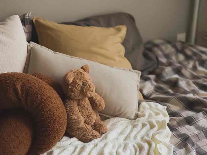 ナチュラルな色調の8畳ワンルーム寝室、枕とブランケットが配置された居心地の良いベッド空間