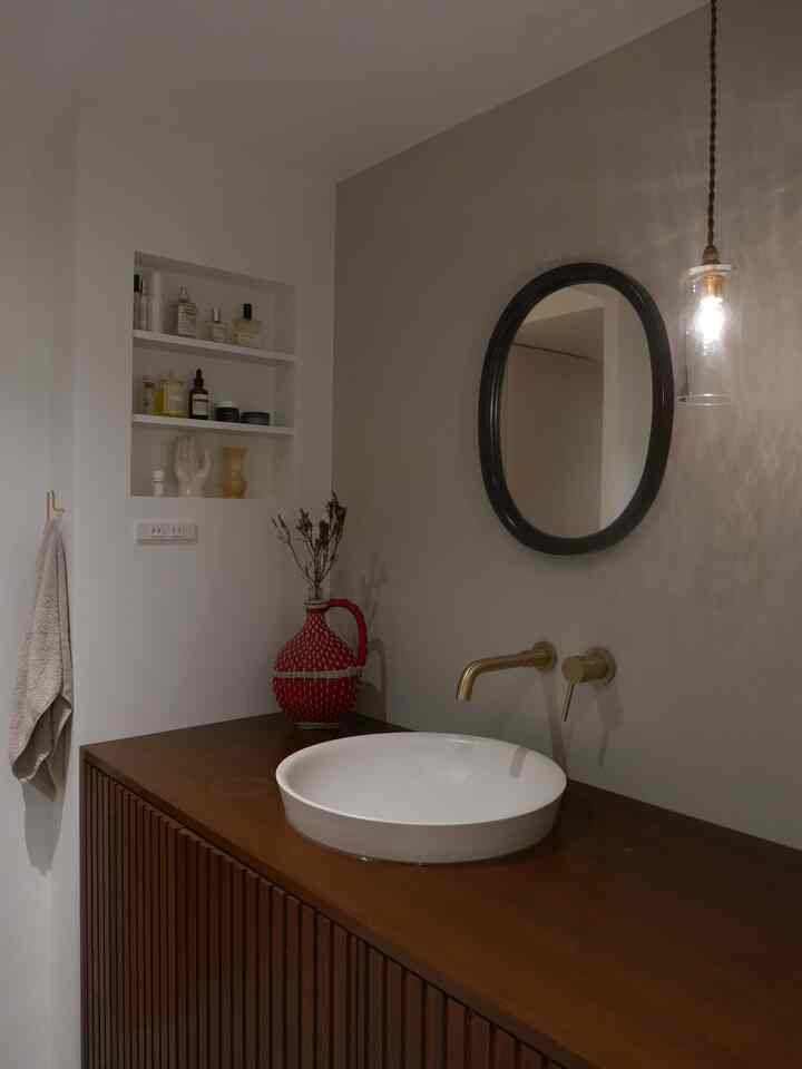 ナチュラルな色調のバスルーム、木製収納と曲木鏡、ペンダントライトが配置された清潔感のあるインテリア