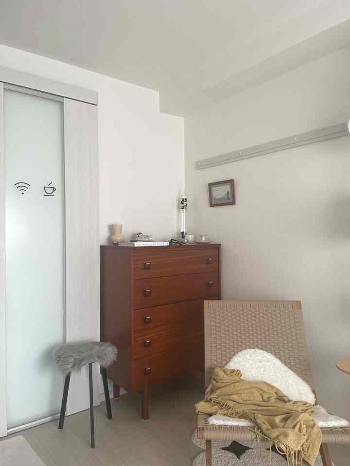 Natural modern living room with white walls and vintage wooden chest, featuring a cozy armchair and stool