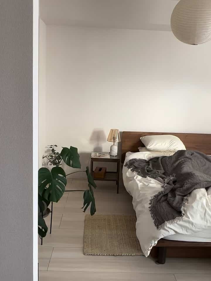 ナチュラルカラーと木目調が特徴の寝室、木製ベッドフレームとナイトテーブル、グレーの寝具と植物が配置された落ち着いた雰囲気のインテリア