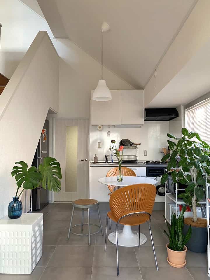 A modern dining room in white and brown tones featuring a dining table, chairs, pendant light, and indoor plants with cozy atmosphere