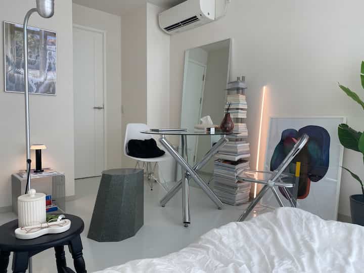 白とシルバーを基調としたミニマルなリビング、ガラスデスクと複数のスツール、壁照明が配置された印象的な空間