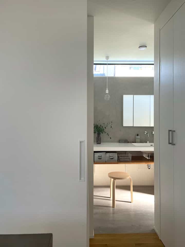 明るい白とナチュラルな木のトーンが調和したバスルーム、化粧台とスツールがすっきり配置されたミニマルなインテリア