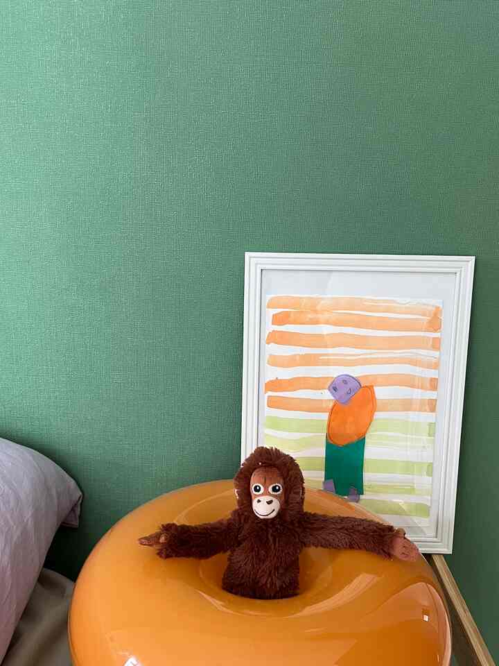 緑色の壁とオレンジ色の照明が調和した子供部屋、子供の絵とオランウータンのぬいぐるみが温かみのある雰囲気を演出