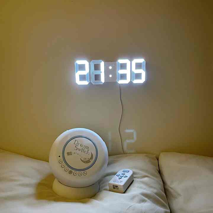 ホワイトトーンの寝室の壁にデジタルLED時計とドリームスイッチプロジェクターが配置された雰囲気のある夜の空間