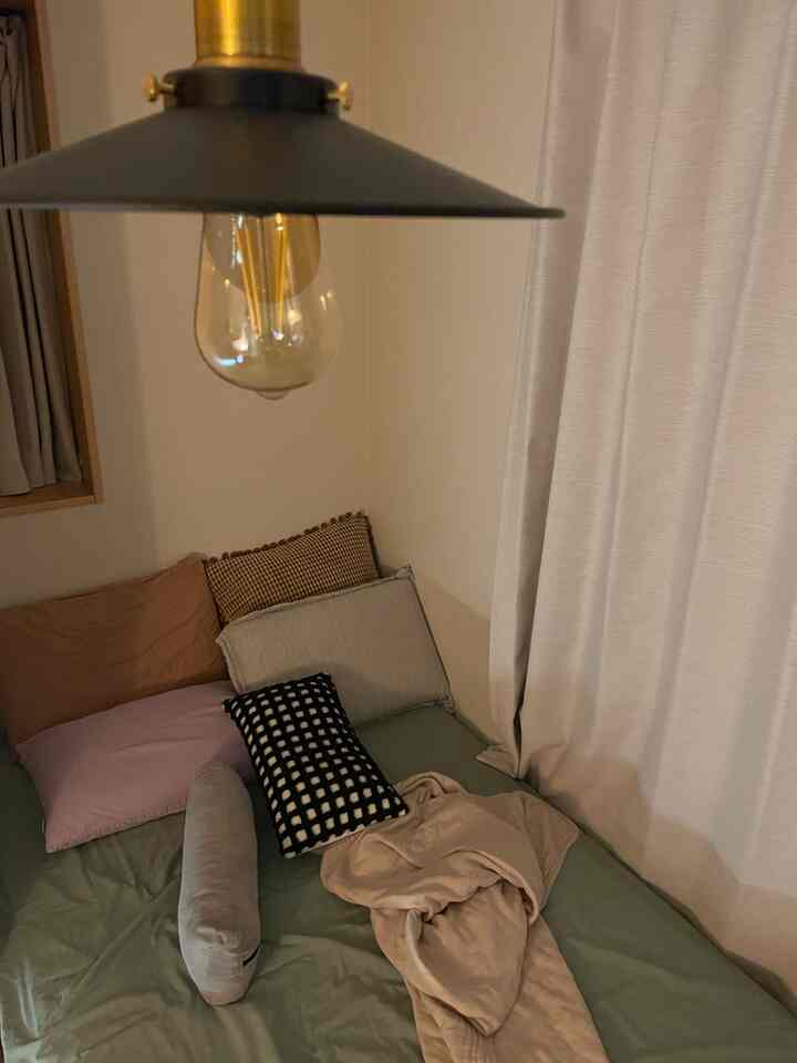 ベージュとグリーンのトーンが特徴的な寝室、クッションとブランケットが配置された雰囲気のある空間