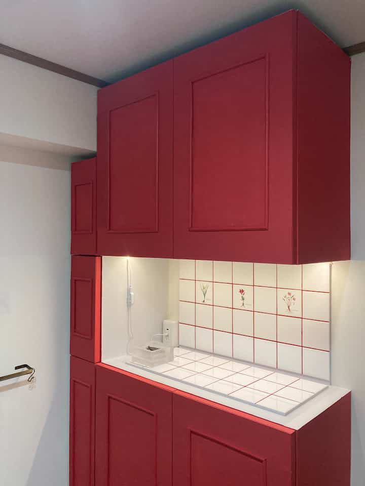Entrance space featuring deep red shoe cabinet with under-cabinet lighting and white tile backsplash decorated with floral motifs, creating a cozy atmosphere