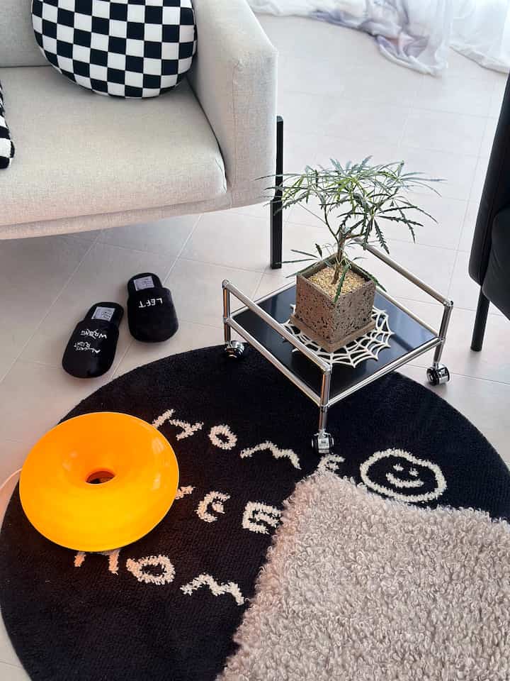 Light-toned living room featuring a white sofa, black round rug, and a potted plant on a mobile plant stand, creating a clean interior